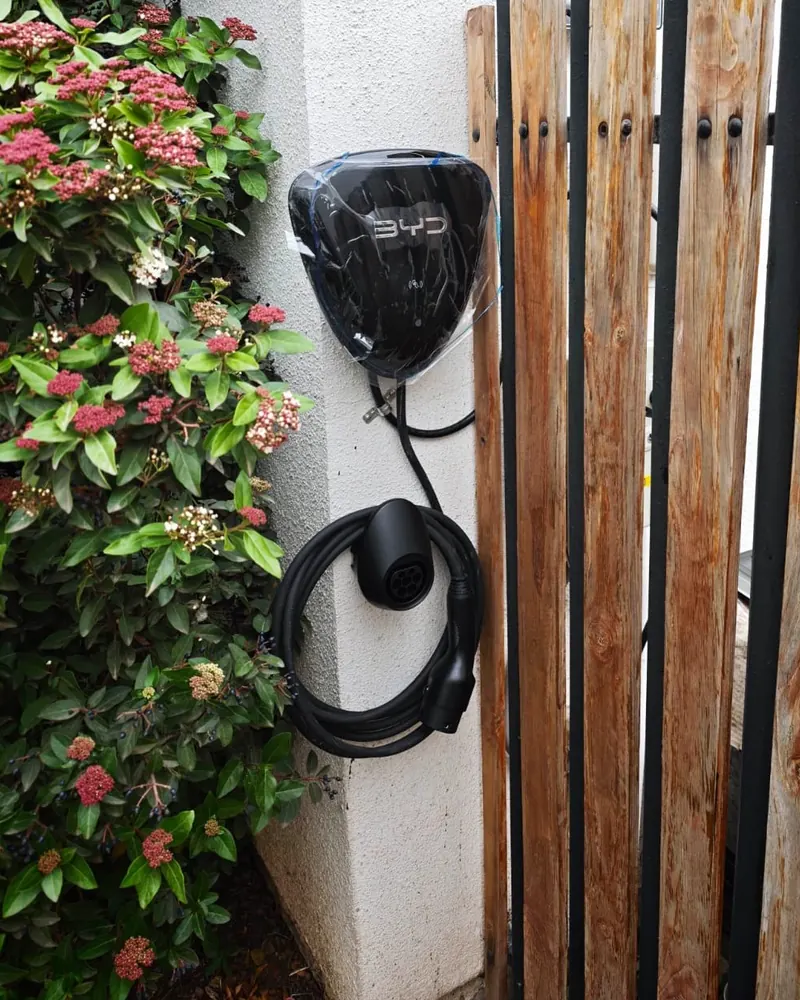 Cargador BYD instalado en el muro de entrada de una casa, junto a un portón de madera