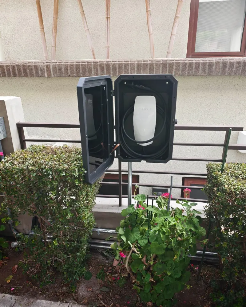 Wall Connector de Tesla dentro de un gabinete protector sobre pedestal en un antejardín