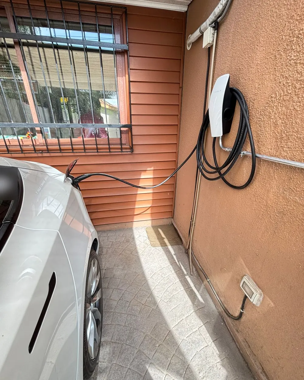 Auto eléctrico cargando con un Wall Connector de Tesla instalado en el muro de una casa